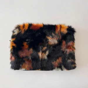 Datorfodral med fuskpäls - handgjort - Datorfodral i svart med silver dragkedja och exklusiv fuskpäls på framsidan – i unika nyanser av svart, orange och beige. På baksidan finns ett svart broderi. Pälsen är 1–2 cm lång och har sytts fast för hand av mig. Passar datorer på max 13 tum. | 🌟Fodralet säljs bara i 1 exemplar och kommer aldrig att återskapas, perfekt om du vill ha något som ingen annan har | 🖐️ Hantverk – tog 3h att skapa | 📏 32×22.5×1.5 cm | 📦 Kan skickas från 29 april | 💬 Hör av dig vid frågor | 🔥Först till kvarn gäller!