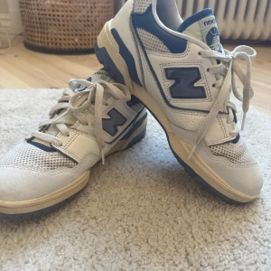 New Balance 550 sneakers i vitt och blått - Säljer ett par New Balance 550 sneakers i vitt och blått. Skorna har mesh och skinnpaneler, snörning och en klassisk retrodesign med blå detaljer och New Balance-logga på sidan.
