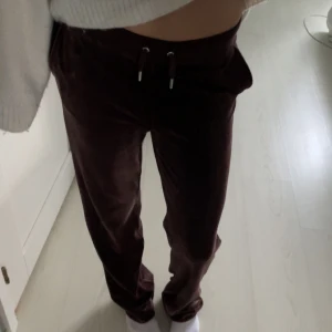 Bruna velourbyxor från Juicy Couture - Mysiga bruna velourbyxor från Juicy Couture med dragsko i midjan och glittrig Juicy-text baktill, men även fickor framtill. Byxorna har raka ben och en liten strassdetalj framtill. Perfekta för en avslappnad och trendig look. (Avända runt 1-2 gånger) SOM NYA!! 