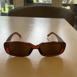 Bruna rektangulära solglasögon - Snygga solglasögon med rektangulära bågar i brun plast. Glasen är tonade och bågarna har en klassisk, stilren design som passar till många olika outfits.