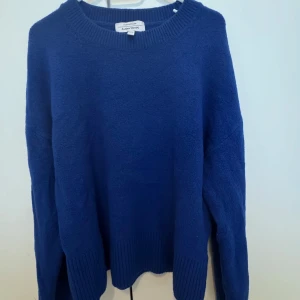 Blå stickad tröja  - Mysig blå stickad tröja från American Vintage med rund halsringning och långa ärmar. Tröjan har breda ribbade muddar vid ärmslut och nederkant, perfekt för lager på lager.