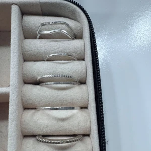 Set med sex silverfärgade ringar - Säljer ett set med sex stilrena ringar i silverfärg. Ringarna har olika former, bland annat vågig design och ringar med små infattade stenar runt om. Perfekta att bära tillsammans eller var för sig för en trendig look.