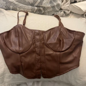 Brun korsett-topp i skinnimitation - Säljer en brun korsett-topp med smala axelband och markerade kupor. Toppen är i skinnimitation. Storlek S