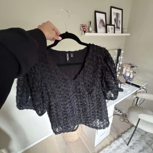 Svart blus - Supersnygg svart blus med v-ringning och korta puffärmar. Hela toppen är täckt av ”3D-blommor”. Köpt på Nelly för 599kr, använd 1 gång. Finns inte längre i svart, säljs bara i vit på Nelly nu.