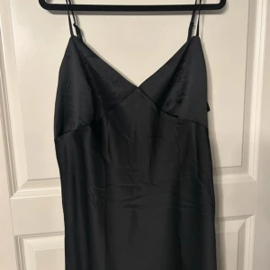 Svart satin klänning med smala axelband - Säljer en svart klänning i satin från H&M. Klänningen har smala axelband och en enkel, elegant design med v-ringad halsringning. Perfekt för dig som gillar stilrena plagg med en lyxig känsla.