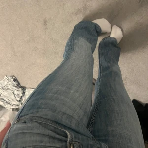 Lågmidjade jeans - Säljer ett par ljusblå bootcut jeans med klassisk femficksdesign och snygga detaljer på bakfickorna. Jeansen har låg midja och ett blommigt innerfoder i linningen. Perfekta för dig som gillar en avslappnad men trendig look.