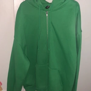 Grön hoodie från H&M med tryck - Aldrig använt, grön hoodie från H&M med vit text 'ADELAIDE RACQUET SPORTS' på ryggen. Tröjan har dragkedja framtill, huva med dragsko och en stor magficka. Perfekt för en sportig och avslappnad stil.
