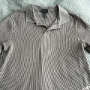 Beige pikétröja från H&M - Säljer en beige pikétröja från H&M i slim fit-modell. Tröjan har korta ärmar, klassisk krage och knappar vid halsen. Materialet är strukturerat och känns mjukt mot huden. Perfekt för en stilren och avslappnad look. Helt oandvänd.