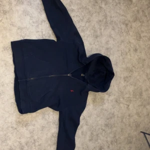 Mörkblå hoodie från Polo Ralph Lauren - Säljer en mörkblå hoodie från Polo Ralph Lauren med dragkedja och klassisk röd logga broderad på bröstet. Tröjan har huva och långa ärmar, perfekt för en avslappnad stil.