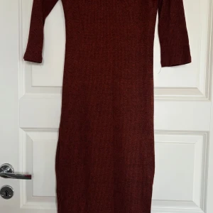 Rostbrun ribbad långklänning - Säljer en rostbrun ribbad långklänning med trekvartsärm och rund halsringning. Klänningen har en smal passform och en liten slits nertill på ena sidan. Perfekt för dig som gillar en enkel men stilren look.