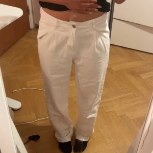 Vita raka jeansbyxor - Säljer ett par vita jeansbyxor med normal passform och raka ben. Klassisk femficksmodell med knapp och dragkedja framtill. Perfekta för en stilren look och lätta att matcha med olika toppar.
