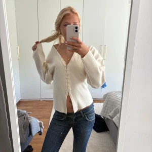 Vit croppad kofta med knappar - Säljer en vit croppad kofta med v-ringning och knappar framtill. Tröjan har lång ärm och är i ett mjukt material, perfekt att styla med jeans eller kjol. Enkel och stilren design som passar till många tillfällen. Använd 1-2 gånger