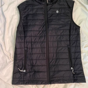 Tunn Svart väst  från 8848 Altitude - Säljer en svart tunn väst från 8848 Altitude med quiltad design och dragkedja framtill. Västen har två fickor med dragkedja och en diskret logga på bröstet. Perfekt för lager-på-lager och stilren look. Pris kan diskuteras vid snabb affär. Köpt för 1200kr