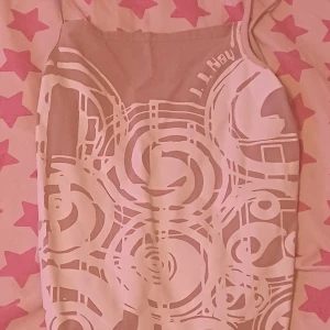 Beige och vit mönstrad tröja med tunna axelband - Säljer ett snygg beige linne med vitt grafiskt mönster och tunna axelband som är från Företaget J.J. Kay. Linnet har en rak passform och är perfekt för varma dagar. Storlek L men passar som M