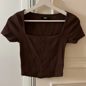 Brun ribbad croppad topp från Bik Bok - Säljer en brun ribbad croppad topp från Bik Bok med fyrkantig ringning och korta ärmar. Perfekt till jeans eller kjol för en enkel och stilren look.