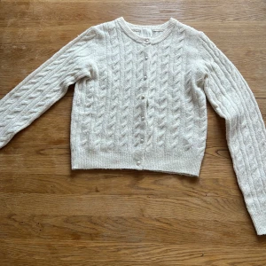 Vit kabelstickad kofta från H&M - Säljer en söt vit kabelstickad kofta från H&M. Koftan har rund halsringning, långa ärmar och knappar framtill. Perfekt att slänga över en topp för en mysig och stilren look. Använt 2 gånger jätte fin men. Behöver sälja ut’ pris kan diskuteras💕  den är xxs men passar xs också för den är strechig💕💕