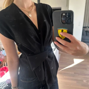 Svart omlottopp med knytband - Säljer en svart omlottopp med snygg knytning i midjan. Toppen har korta ärmar och en djup v-ringning framtill. 