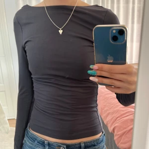Mörk grå långärmad topp med djup rygg - Säljer en mörk grå långärmad topp i stretchigt material. Toppen har en tight passform och en djup, rundad urringning i ryggen. Perfekt att styla med jeans eller kjol för en snygg look.