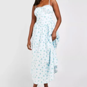 Blommig långklänning från Boohoo - Superfin långklänning från Boohoo med smala axelband och blått blommönster på vit botten, spets längst upp vid brösten. Använd endast 1 gång, säljs på grund av att jag inte använder den.