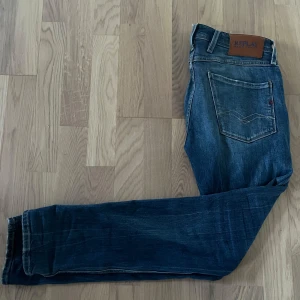 Blå Replay Anbass jeans 573 Bio - Säljer ett par blå Replay Anbass jeans, modell 573 Bio. Jeansen har klassisk femficksdesign, läderpatch bak och snygga slitningar på fickorna. Passformen är slim och materialet är denim. Perfekta för dig som gillar stilrena jeans med modern känsla. Jeansen är använda fåtal gånger😃