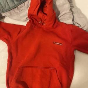 Röd hoodie från Prada - Säljer en snygg röd hoodie från Prada med klassisk logga på bröstet. Tröjan har huva med dragsko och en stor magficka framtill. Perfekt för dig som vill ha något stilrent men ändå sticker ut.