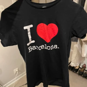 Svart t-shirt med I Love Barcelona-tryck - Svart t-shirt i 100% bomull från THK med trycket 'I ♥ Barcelona' på bröstet. Klassisk passform och rund halsringning. Perfekt för dig som älskar Barcelona eller vill ha en statement-tee.