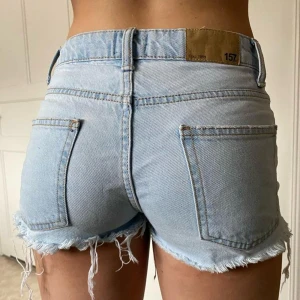 Ljusblå jeansshorts med fransar - Säljer ett par ljusblå jeansshorts från 157 med råa fransade kanter och klassisk femficksdesign. Shortsen har bälteshällor och knappgylf. Perfekta för varma dagar och en avslappnad stil.