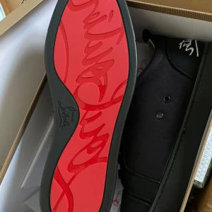 Loubs - Snygga helsvarta sneakers från Christian Louboutin med svart snörning och diskret logga broderad i vitt på hälen. Skorna har rund tå och platt sula, tillverkade i mocka och syntetmaterial. Perfekta för en stilren look.