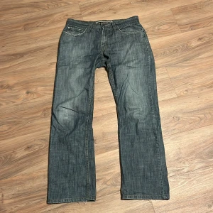 Levis 514 blå jeans - Klassiska blå Levis 514 jeans med raka ben och fem fickor. Byxorna har knappgylf och synliga slitningar vid benslut. Ikonisk Levis-lapp bak i midjan och röd Levis-tagg på bakfickan.