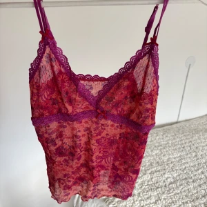  spetslinne med blommigt mönster - Säljer ett vackert spetslinne med blommigt mönster. Den är orange och rosa. Linnet har justerbara axelband och en söta rosett framtill. Perfekt för att lägga till en romantisk touch till din outfit. Jag säljer den då jag aldrig andvönt den och den är inte riktigt min stil. På bild 5 ser man att den är en aning genomskinligt men inget som märks på tydligt när man provar den. 😊😊