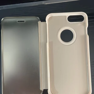 Guldigt mobilfodral med spegel - Snyggt guldigt mobilfodral med spegel på insidan. Fodralet har en praktisk öppning för kameran och kan ställas upp för handsfree-användning. Perfekt för att skydda din mobil med stil.