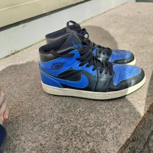 Nike Air Jordans i svart och blått - Säljer ett par klassiska Nike Air Jordans i svart och blått. Skorna har en hög modell med snörning och en ikonisk design. Perfekta för sneaker-entusiaster som vill ha en stilren look.