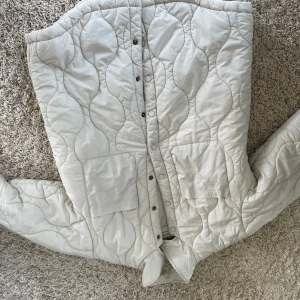 Vit quiltad jacka från Samsøe Samsøe - Säljer en stilren vit quiltad jacka från Samsøe Samsøe. Jackan har knappar framtill och en snygg quiltad design som ger en modern look. Perfekt för kyligare dagar. Använt fåtal gånger. Passar även de som har en mindre st. 