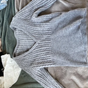 Grå ribbad tröja - Säljer en stilren grå ribbad tröja med v-ringning. Tröjan har långa ärmar och är perfekt för kyligare dagar. Passar bra till både jeans och kjol.