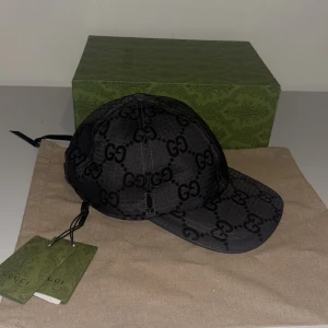 Svart keps från Gucci - Snygg svart keps från Gucci med det ikoniska GG-mönstret. Kepsen har en justerbar rem baktill för perfekt passform och kommer med originalförpackning och etiketter. Perfekt för att ge din outfit en lyxig touch.
