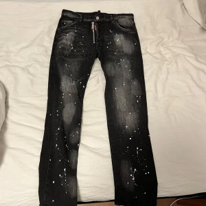 Svarta jeans med stänkmönster från Dsquared2 - Snygga svarta jeans från Dsquared2 med unikt stänkmönster. Byxorna har en dragkedja och knapp framtill samt en cool detalj med Dsquared2-logga vid fickan. Perfekta för dig som vill sticka ut med en edgy stil. Pris sänks vid snabbaffär.
