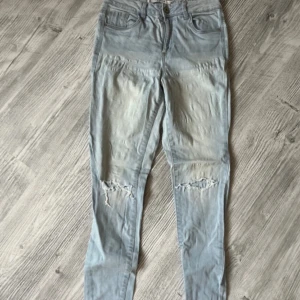 Ljusblå jeans från Lefties 36 - Säljer ett par ljusblå jeans från Lefties med slitna detaljer på knäna. De har en dragkedja och knapp framtill samt fem fickor. Perfekta för en avslappnad stil. Storlek 36