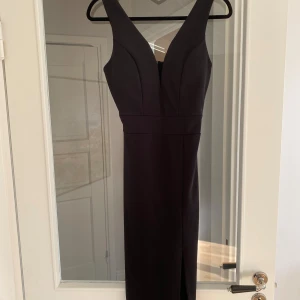 Svart midiklänning med slits - Elegant svart midiklänning med djup v-ringning och  slits framtill. Fodrade kupor vid bysten. Använd en gång. 