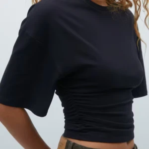 Svart kortärmad topp med rynkdetalj - Snygg svart kortärmad topp med rynkdetalj på sidorna. Perfekt för en stilren look. Tillverkad i mjukt material för extra komfort.