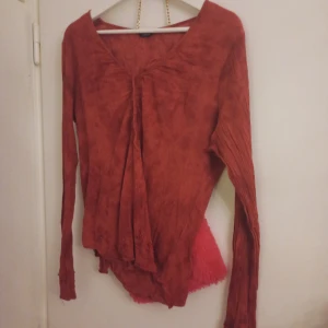 Rostfärgad långärmad blus - Säljer en snygg rostfärgad blus med långa ärmar och v-ringad design. Perfekt för en stilren look. Blusen har en unik textur och en lös passform som ger en bekväm känsla.