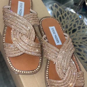 Glittriga sandaler från Steve Madden - Snygga sandaler från Steve Madden med glittriga detaljer i guld. De har en korsad design över foten och en bekväm sula. Perfekta för att ge en touch av glamour till din outfit. Storlek 36