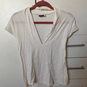 Vit v-ringad topp  - Säljer en stilren vit v-ringad topp från Add It. Toppen har korta ärmar och är tillverkad i ett mjukt material som ger en skön passform. Perfekt för en avslappnad look. Hör av dig vid intresse!