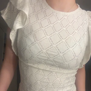 Vit blus med volangärmar - Säljer en söt vit blus med volangärmar och ett diskret rutmönster. Blusen har en tight passform och är perfekt för både vardag och fest. 