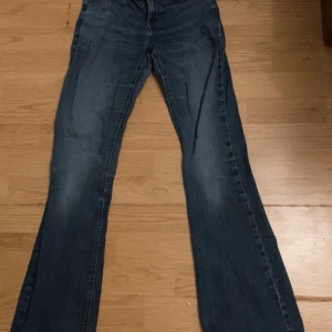 Blå bootcut jeans från Lindex - Säljer ett par blå bootcut jeans från Lindex. De har en klassisk femficksdesign och en liten reva på ena benet. Perfekta för en avslappnad stil.