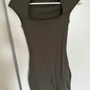 Mörk grön klänning med fyrkantig urringning - Säljer en stilren grön klänning med fyrkantig urringning och korta ärmar. Perfekt för en enkel och elegant look. Klänningen har en tight passform som framhäver figuren. Hör av dig innan du köper!