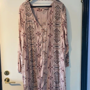 Mönstrad klänning från Culture - Säljer en mönstrad klänning från Culture i storlek L. Klänningen har ett detaljerat mönster i svart och rosa på en ljus bakgrund. Den har en v-ringad hals och långa ärmar, perfekt för både vår och höst.