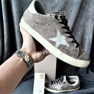 Golden Goose - Snygga grå sneakers från Golden Goose i mocka med vit stjärndetalj på sidan. Skorna har svarta snören och en vit sula som ger en cool kontrast. Perfekta för en avslappnad stil. Box medföljer. 