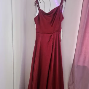 Vinröd satin klänning - Elegant vinröd långklänning i satin med knytband vid axlarna. Perfekt till event som skolbal och mm. Använd 1 gång men i jättebra skick. Skriv gärna för fler bilder💘