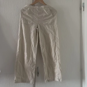 Beige byxor från Kappahl - Säljer ett par beige byxor från Kappahl. Byxorna har en loose passform med hög midja och stora fickor framtill. Perfekta för en avslappnad stil.