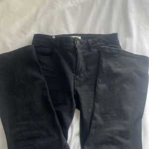 Svarta jeans från Lindex - Snygga svarta jeans från Lindex i klassisk design. De har en knapp och dragkedja framtill samt fickor både fram och bak. Perfekta för en stilren look.